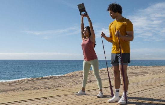 imagem de um casal na praia com acessórios de reforço muscular a realizar exercicio fisico