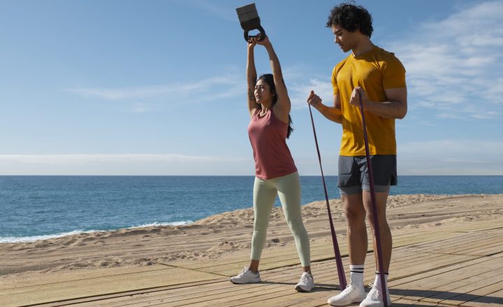 imagem de um casal na praia com acessórios de reforço muscular a realizar exercicio fisico