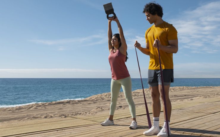 imagem de um casal na praia com acessórios de reforço muscular a realizar exercicio fisico