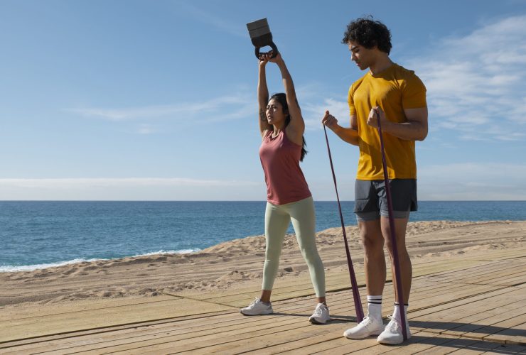 imagem de um casal na praia com acessórios de reforço muscular a realizar exercicio fisico